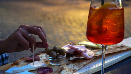Close up of italian appetizers and spritz table with woman's hand taking olive from the plate,...
