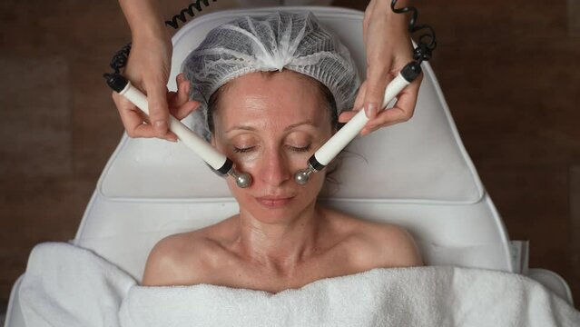 Beautiful 40s middle aged female receiving facial microcurrent therapy at cosmetology clinic. Non surgery, hardware cosmetology, anti-age rejuvenation skincare concept. High quality 4K footage