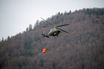 Helicopter with water bucket ready for extinguishing wildfire area in mountains