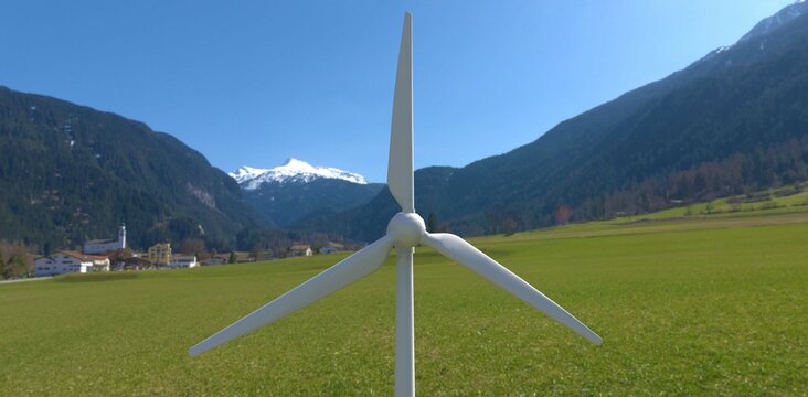 The blades of an industrial wind turbine against the backdrop of a mountain village. Renewable energy plus self-contained power supply. 3d render.
