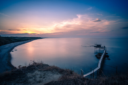 il tramonto sul trabocco di punta aderci, a vasto. il sole cala nell'entroterra abruzzese, dietro il gran sasso, e colora le nuvole ed il trabocco simbolo del parco. foto in lunga esposizione