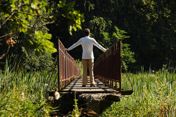 Young man in a white shirt standing on a narrow bridge. Pavel Kubarkov, i on narrow bridge and summer nature around me. Photo was taken 24 August 2022 year, MSK time in Russia. - 530175727