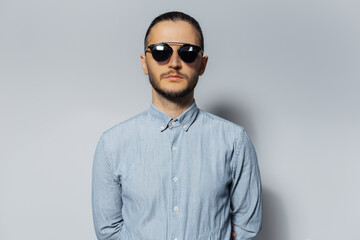 Studio portrait of young serious man wearing sunglasses and blue shirt on white background.