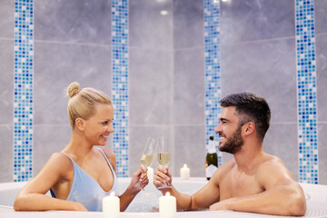 Romantic couple toasting in a hot tub in spa center. A happy romantic married couple sitting in a hot tub in wellness and spa center and toasting with champagne.