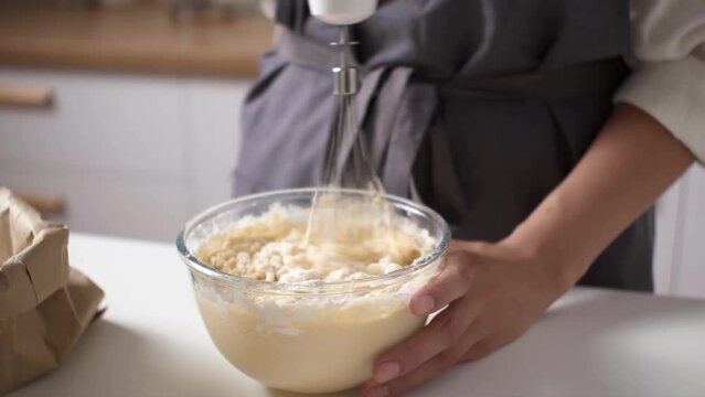 Process of making dough for pancakes with flour in paper bag on light table, eggs, flour  beat with mixer. Pancake dough with ingredients beat mixer. Woman beats dough at kitchen table in kitchen
