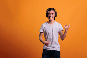 Young asian man in headphones playing virtual guitar, imagining rockstar lifestyle. Musician...