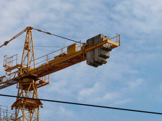Close-up photo of a yellow tower crane with a cloudy sky in the background	