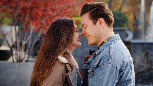 Gentle caucasian boyfriend man caress loved girlfriend woman talk about future outdoors stand closeness rub noses touch each other on romantic date couple partners young lovers cuddle in autumn park