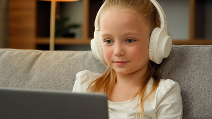 Funny little blonde girl child cute schoolgirl pretty beautiful kid young blogger wears headphones...