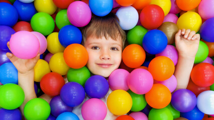 Fototapeta na wymiar Smile kid lying colorful plastic balls pool. Colorful balls dry pool kindergarten playground child indoor play area. Playroom kids ball pit. Caucasian boy indoor playground kids play zone or kids zone