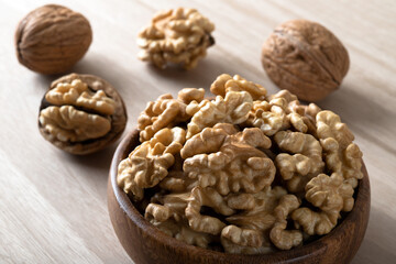 Peeled walnuts and whole walnuts in wooden bowl
