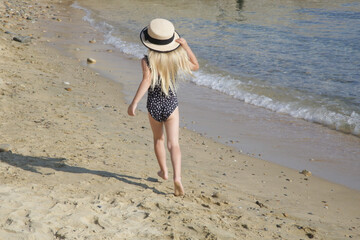 Adorable toddler girl in black swimsuit and straw hat enjoying a day at the beach. Idyllic summer...