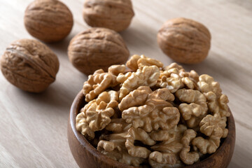 Peeled walnuts and whole walnuts in wooden bowl