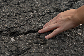 Large cracks in the asphalt the size of a man's hand. A close-up of the woman stuck her fingers in a huge crack in the ground. defects from the operation of the road surface.