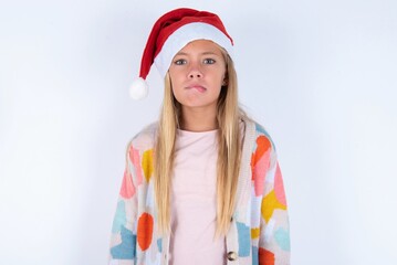 little kid girl with Christmas hat wearing yarn jacket over white background making grimace and crazy face, screaming out of control, funny lunatic expressing freedom and wild.