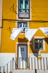 Yellow house with white drying laundry on beautiful old cozy street in Lisbon, Portugal.
