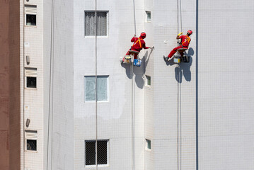 Trabalhadores da construção civil fazendo manutenção predial por meio de rapel