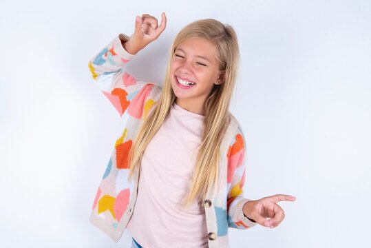 Photo of upbeat little kid girl wearing colorful yarn jacket over white background has fun and dances carefree wear being in perfect mood makes movements. Spends free time on disco party