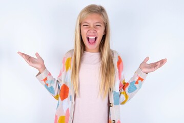 Crazy outraged little kid girl wearing colorful yarn jacket over white background screams loudly...