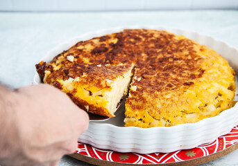 Persona tomando un trozo de torta española con fondo blanco de ladrillos