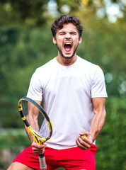A young handsome male Caucasian tennis player, happy winning, celebrates a victory after winning a...