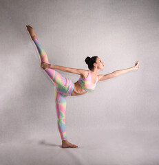 A beautiful slender gymnast in a tracksuit does sports or yoga in the studio in the swan pose