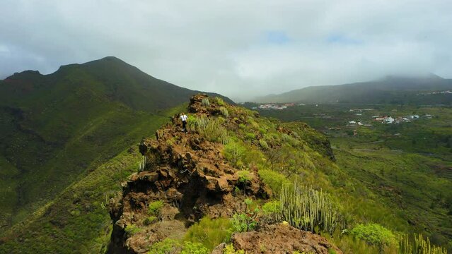 Attractive woman walking in dangerous mountain. Pretty girl runs along path on cliff. Cactus bushes, rocky volcanic landscape. Aerial. Athlete, hill ridge. Tamaimo. Way, Risco Blanco. Tenerife.