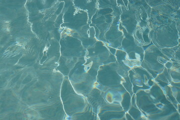 Kleine Wellen in einem mit Wasser gefüllten Pool reflektieren und spiegeln das helle Tageslicht; sie erzeugen irreguläre Muster. Die Wellen werden durch Kinder und den Wind erzeugt.  - obrazy, fototapety, plakaty