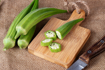 pieces of chopped okra on a cutting board with a knife. On the background of burlap. - obrazy, fototapety, plakaty
