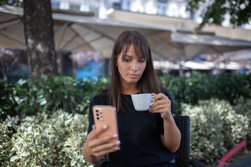 Morning in cafe - attractive woman in black drinkin coffe and make selfie photo for social networks