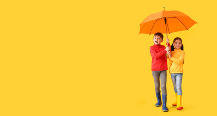 Cute little children in autumn clothes and with umbrella on yellow background with space for text