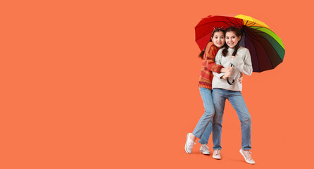 Portrait of cute twin girls with umbrella on orange background with space for text