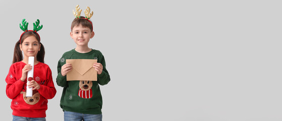Funny little children with reindeer horns and letters to Santa on light background with space for text