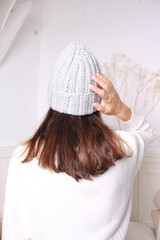 An unrecognizable young girl demonstrates a knitted hat in a bright room. Fashionable knitted hats autumn-winter.Back view.