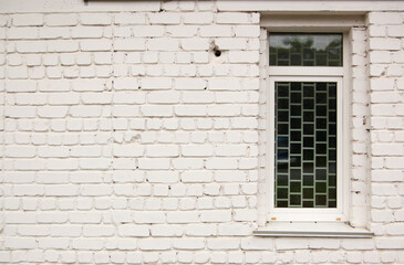 Fototapeta na wymiar Brick white painted wall with a narrow glazed window