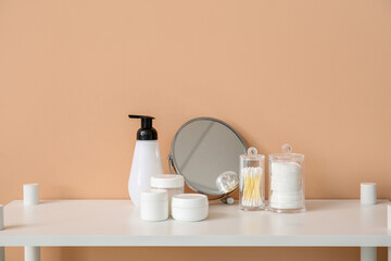 Fototapeta na wymiar Mirror and different bath accessories on table near beige wall