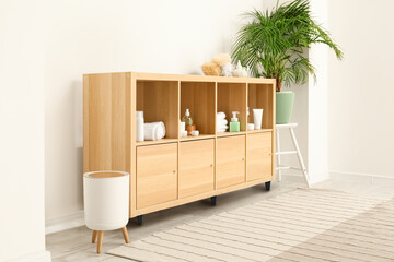 Shelf unit with different bath accessories and houseplant near white wall in bathroom interior