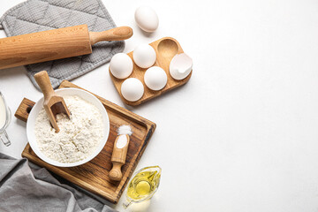 Fototapeta na wymiar Bowl of flour, eggs, oil and rolling pin on light background