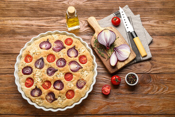 Baking dish with tasty Italian focaccia and ingredients on wooden background