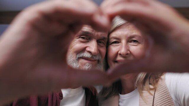 Demonstration of love and sincere feelings of a beautiful, elderly gray-haired couple. A close-up portrait of happy pensioners showing their hearts as a sign of many happy years together.