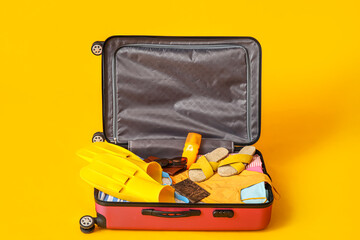 Open suitcase with beach accessories and passport on yellow background