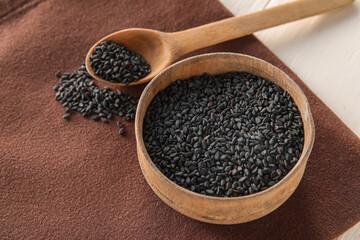 Wooden bowl and spoon of black sesame seeds on table, closeup