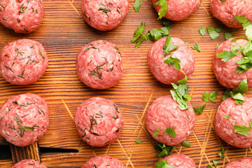 Raw meat balls with cut herbs on wooden board, closeup