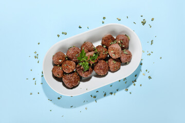 Plate with tasty meat balls and herbs on blue background