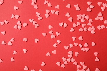 Bright heart shaped sprinkles on red background, flat lay