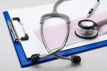 Stethoscope, clipboard and cardiogram paper on white background, closeup