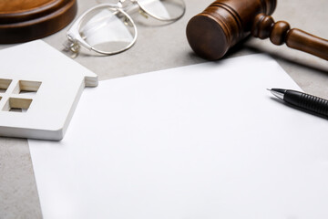Last will and testament near house figure, glasses and gavel on light grey table, closeup