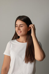 Fototapeta premium Happy young woman touching her hair on light background
