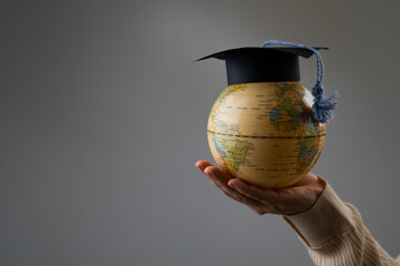 Woman holding a globe wearing a graduation cap. 
