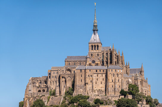 Mont St. Michel, Normandy, France - July 8, 2022: closeup of brown stone religious part, abbay and church on its rock against blue sky.